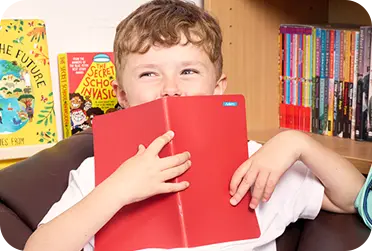 Child holding red notebook with name label on it in front of his face
