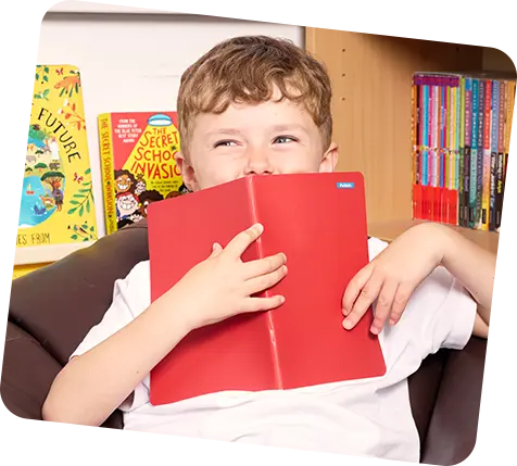 Child holding red notebook with name label on it in front of his face