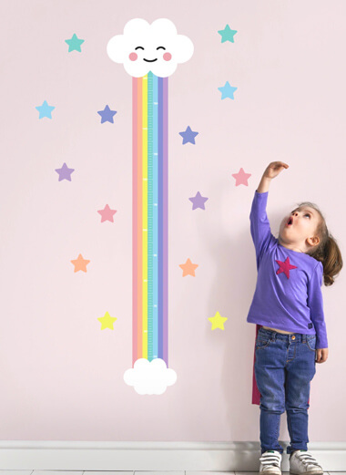 My Nametags rainbow cloud height chart on a pink wall with a little girl standing next to it